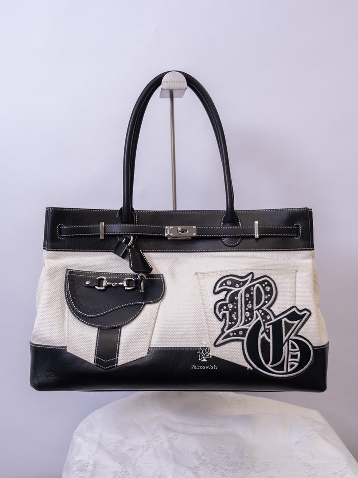 Black and white canvas leather tote with large embroidered initial patch and pocket detail.