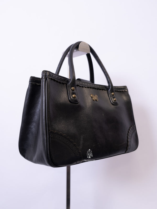 Anna Sui black leather mini tote bag with butterfly emblem and scalloped corner stitching.