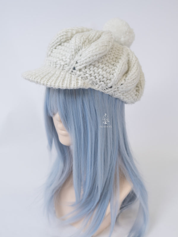 Chunky white knitted newsboy cap with a large pom-pom and ribbed brim.