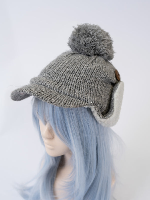 Side view of a grey knit trapper-style cap with a pom-pom, wooden button detail, and sherpa-lined earmuffs.