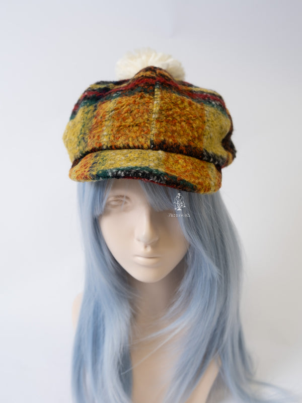 Multicolor plaid wool newsboy cap with cream pom-pom on top.