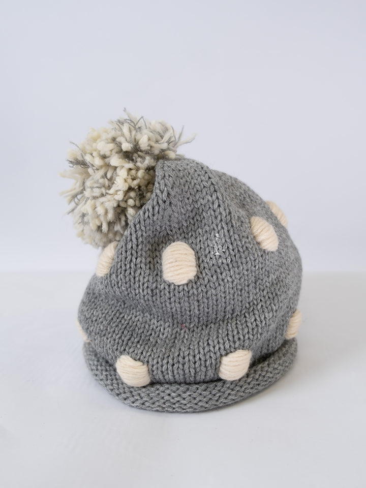 Grey chunky knit hat with cream dot details and a mixed-yarn pom-pom on top.