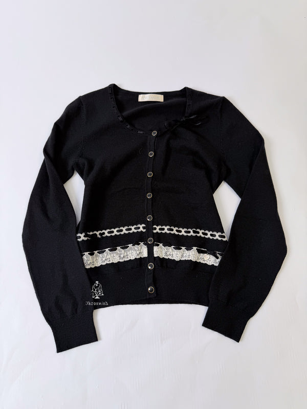 Black knit cardigan with white lace trim and decorative ribbon details.